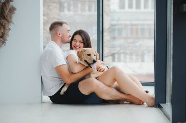 Mutlu Aile Kavramı. Modern apartmanda yerde oturan köpekli güzel bir çiftin portresi.