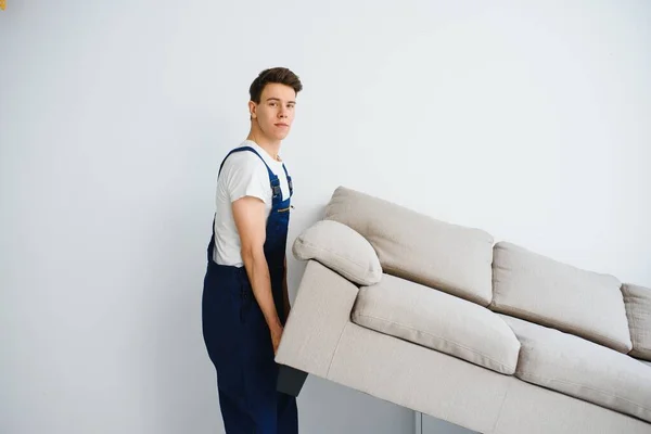 Loader moves sofa, couch. worker in overalls lifts up sofa, white background. Delivery service concept. Courier delivers furniture in case of move out, relocation.