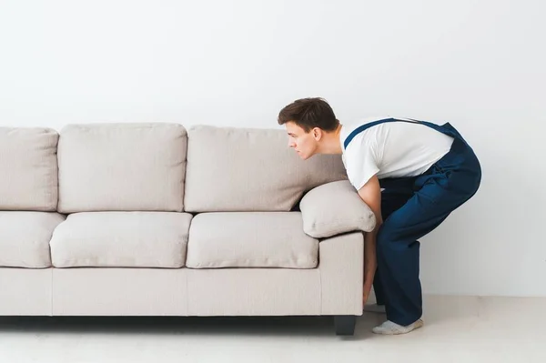 Loader moves sofa, couch. worker in overalls lifts up sofa, white background. Delivery service concept. Courier delivers furniture in case of move out, relocation.