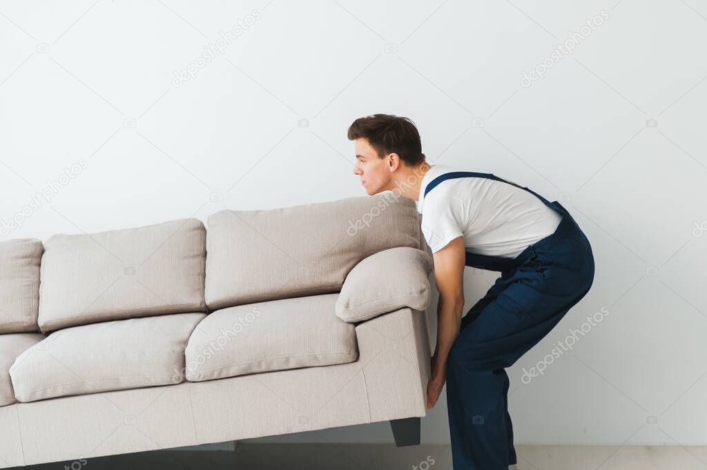 Loader moves sofa, couch. worker in overalls lifts up sofa, white background. Delivery service concept. Courier delivers furniture in case of move out, relocation.