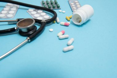 Mavi masaya saçılmış beyaz haplar. Tıbbi, eczane ve sağlık sigortası konsepti. Mavi arka plan beyaz haplar, tıbbi statoskop, üst görüş..