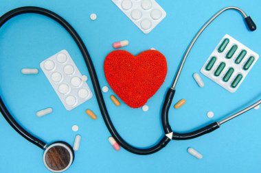 Bir kalp ve steteskop yakın plan mavi arka plan, üst manzara. Küresel sağlık hizmeti kavramı. Kalp sağlığıyla ilgilenmek. Tabletler ve ampullerle tedavi