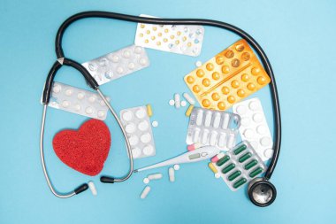 İlaçlar, iş aletleri ve aksesuar doktoru, hemşire. Tıbbi set - tabletler, termometre, şırınga, ampul, yapıştırıcı sıva ve mavi arka planda statoskop. Düz yatıyordu