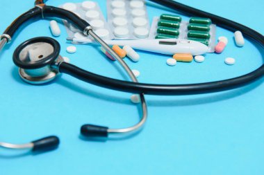 Mavi masaya saçılmış beyaz haplar. Tıbbi, eczane ve sağlık sigortası konsepti. Mavi arka plan beyaz haplar, tıbbi statoskop, üst görüş..