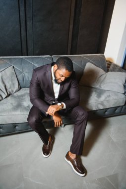 Siyah takım elbiseli genç bir adam bir kanepede oturuyor. Genç bir adamın moda portresi..