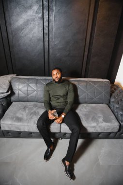 Yakışıklı, Afro-Amerikalı, şık takım elbiseli, kanepede dinlenen bir bardak viskiyle.