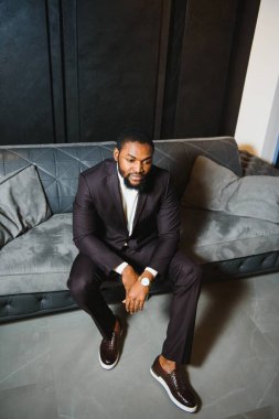 Siyah takım elbiseli genç bir adam bir kanepede oturuyor. Genç bir adamın moda portresi..