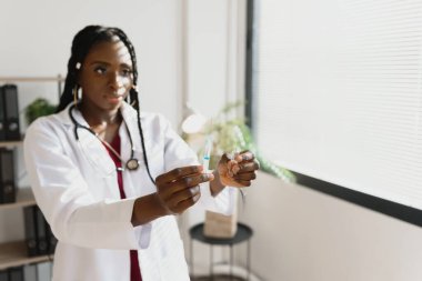 Genç Afro-Amerikalı kadın doktorun elinde şırıngayla hastanede iğne yapmaya hazır olduğunu gördüm.