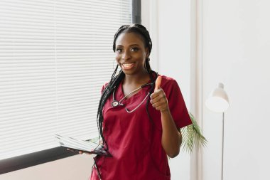 Hastane ofisinde steteskoplu beyaz önlüklü gülümseyen kadın doktor portresi.