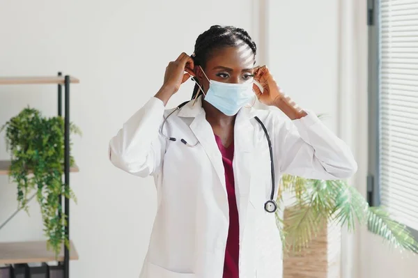 medicine, profession and healthcare concept - african american female doctor or scientist in protective facial mask in clinic