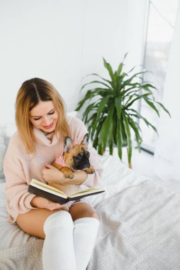 Köpeği ve kitabı olan genç bir kadın evde oturup kitap okuyor..