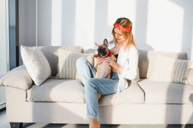 Neşeli genç bir kadın siyah burunlu köpeğini tutuyor ve gülüyor. Fransız buldoguyla poz veren gülümseyen kızın kapalı bir portresi.