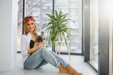 Güzel sarışın kadın evde köpeğiyle oynuyor, gülümsüyor. Mutluluk.