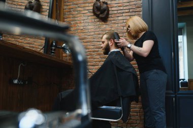 Şık bir adam berber dükkanında kuaför kadın saçını kesiyor yakışıklı, sakallı, beyaz bir adam moda saç kesimi yaptırıyor çekici berber kız müşteriye hizmet ediyor.