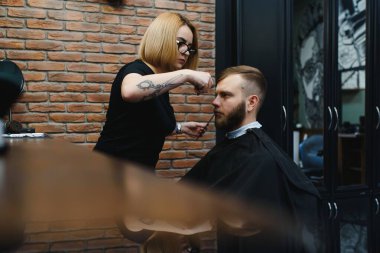 Profesyonel kuaför kadın berber dükkanında elektrikli saç makasıyla yakışıklı adamın stilini yapıyor.