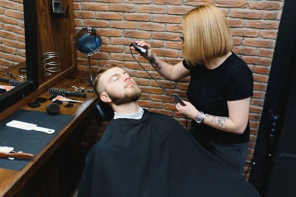 Woman barber cutting hair to a bearded man.
