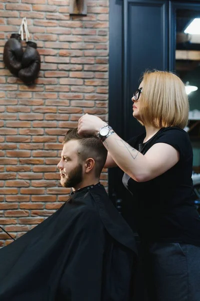 Woman barber cutting hair to a bearded man.