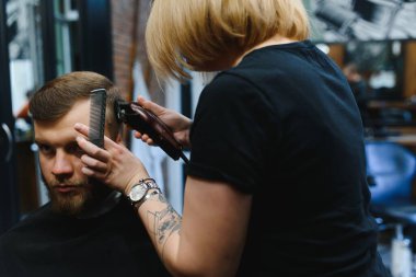 Şık bir adam berber dükkanında kuaför kadın saçını kesiyor yakışıklı, sakallı, beyaz bir adam moda saç kesimi yaptırıyor çekici berber kız müşteriye hizmet ediyor.