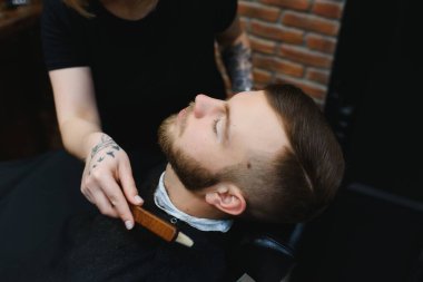 Berber dükkanı ya da kuaför konsepti. Kadın kuaför sakalı makasla keser. Uzun sakallı, bıyıklı ve şık saçlı bir adam. Modern saç stili olan adam kuaförü ziyaret ediyor.