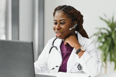Portatif bilgilendirme cihazı kullanarak ofisinde çalışan Afrikalı Amerikalı kadın doktor. Teletıp hizmetleri. Ana bakım danışmanlıkları, psikoterapi, acil servisler..