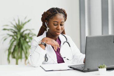 Tıp, internet hizmeti ve sağlık konsepti - Mutlu gülümseyen Afro-Amerikan kadın doktor veya kulaklık ve dizüstü bilgisayarlı hemşire hastanede konferans veya video görüşmesi yapıyor