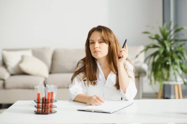 Ofis masasında çalışan kadın doktor, arka planda ofis içi.