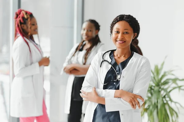health care, profession, people and medicine concept - happy african american female doctor or nurse over group of medics meeting at hospital