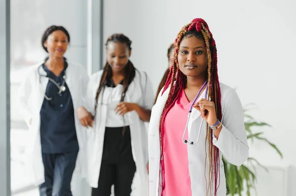 health care, profession, people and medicine concept - happy african american female doctor or nurse over group of medics meeting at hospital