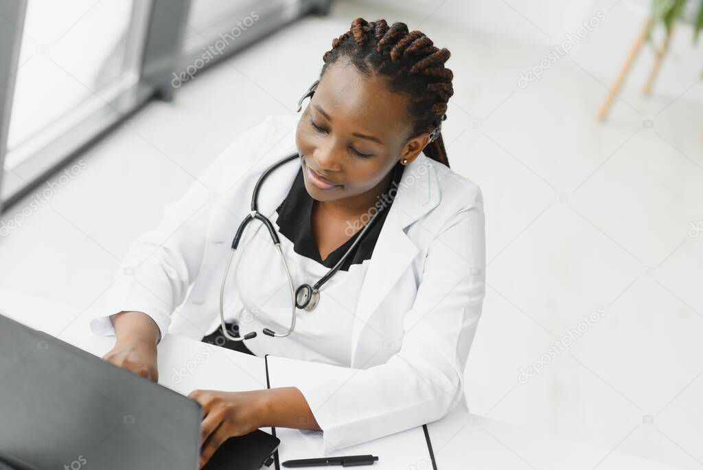 African American woman doctor working at her office online using portable inormation device. Telemedicine services. Primary care consultations, psychotherapy, emergency services.