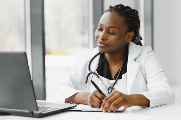 medicine, online service and healthcare concept - happy smiling african american female doctor or nurse with headset and laptop having conference or video call at hospital