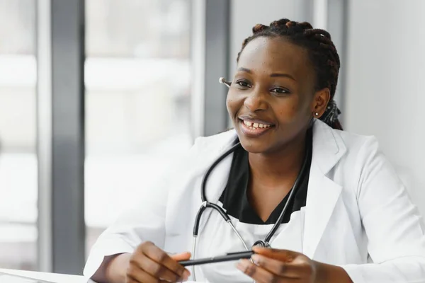 medicine, online service and healthcare concept - happy smiling african american female doctor or nurse with headset and laptop having conference or video call at hospital