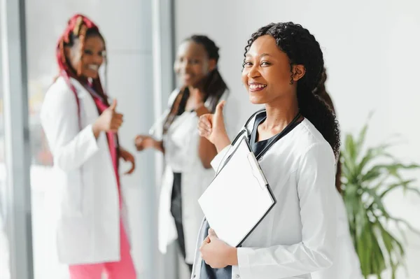 health care, profession, people and medicine concept - happy african american female doctor or nurse over group of medics meeting at hospital