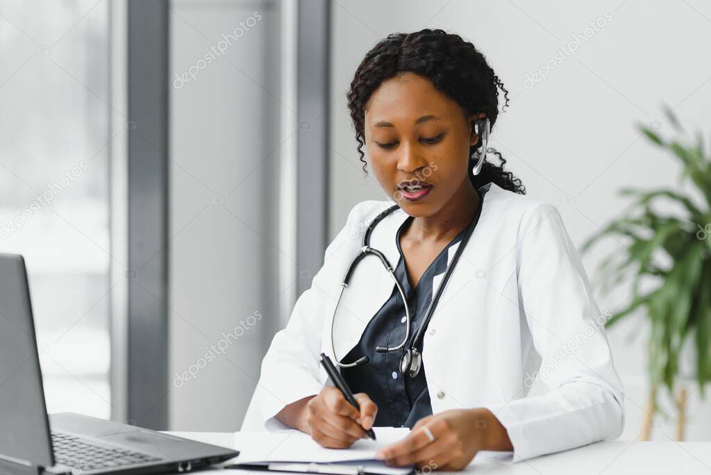African American woman doctor working at her office online using portable inormation device. Telemedicine services. Primary care consultations, psychotherapy, emergency services.