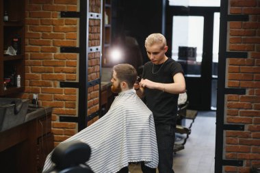 Genç yakışıklı berber berber dükkanında sakallı çekici bir adamın saçını kesiyor.