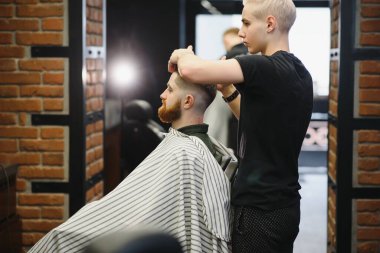 Berber dükkanı. Berber koltuğunda bir adam, kuaför saçını şekillendiriyor.