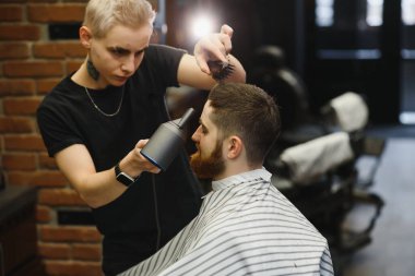 Genç yakışıklı berber berber dükkanında sakallı çekici bir adamın saçını kesiyor.