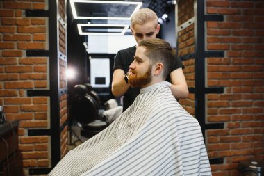 Genç yakışıklı berber berber dükkanında sakallı çekici bir adamın saçını kesiyor.