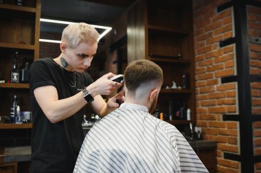 Genç yakışıklı berber berber dükkanında sakallı çekici bir adamın saçını kesiyor.