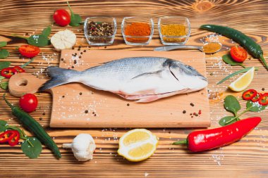 Limon, biber, domates ve ahşap zemin üzerinde kopya alanı olan çeşitli baharatlarla birlikte taze çiğ dorado balığı..