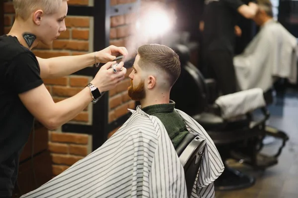 Berber dükkanı. Berber koltuğunda bir adam, kuaför saçını şekillendiriyor.