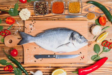Taze çiğ dorado balığı. Çipura, ahşap bir tahtanın üzerinde, otlar, tuz ve baharatla birlikte. Dorado ve masada yemek pişirmek için malzemeler. Yakın plan.