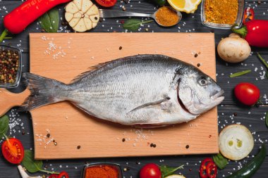 Limon, biber, domates ve ahşap zemin üzerinde kopya alanı olan çeşitli baharatlarla birlikte taze çiğ dorado balığı..