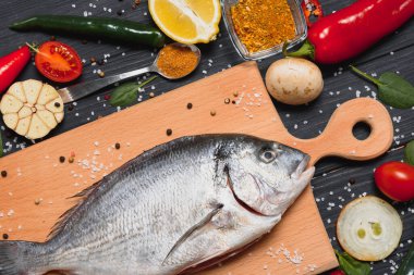 Taze çiğ dorado balığı. Çipura, ahşap bir tahtanın üzerinde, otlar, tuz ve baharatla birlikte. Dorado ve masada yemek pişirmek için malzemeler. Yakın plan.