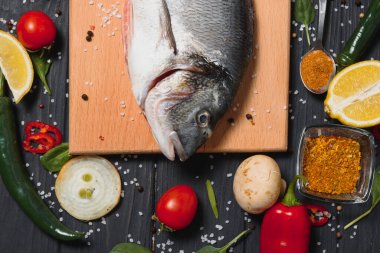 Limon, biber, domates ve ahşap zemin üzerinde kopya alanı olan çeşitli baharatlarla birlikte taze çiğ dorado balığı..