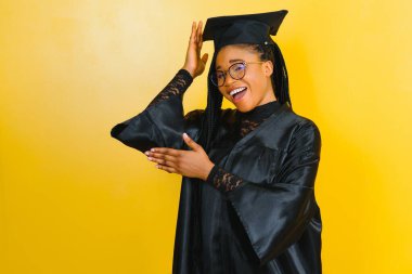 Mezuniyet şapkası ve cübbesi içinde okul binasının önünde güzel bir Afrikalı üniversite öğrencisi.