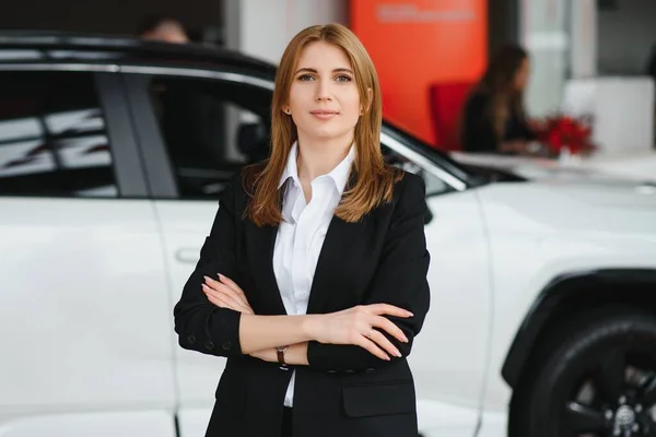 Young woman consultant in show room standing near car