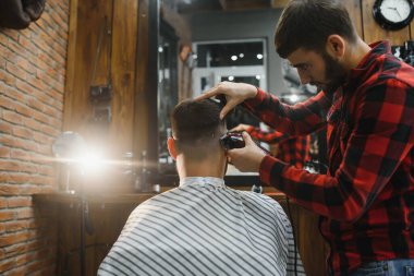 Yakışıklı sakallı adam kuaförde saçını kestirirken gülümsüyor.