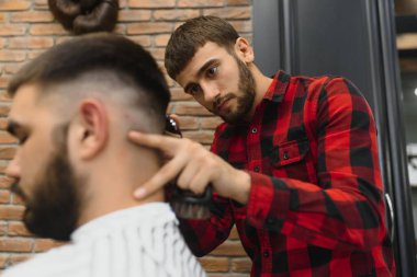 Saç kesimini mükemmel gösteriyor. Genç sakallı adam berber dükkanında sandalyede otururken kuaför tarafından tıraş oluyor.