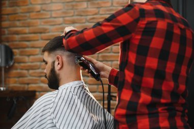 Saç kesimini mükemmel gösteriyor. Genç sakallı adam berber dükkanında sandalyede otururken kuaför tarafından tıraş oluyor.