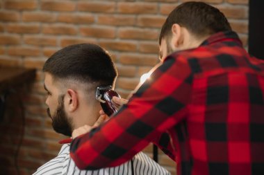 Saç kesimini mükemmel gösteriyor. Genç sakallı adam berber dükkanında sandalyede otururken kuaför tarafından tıraş oluyor.